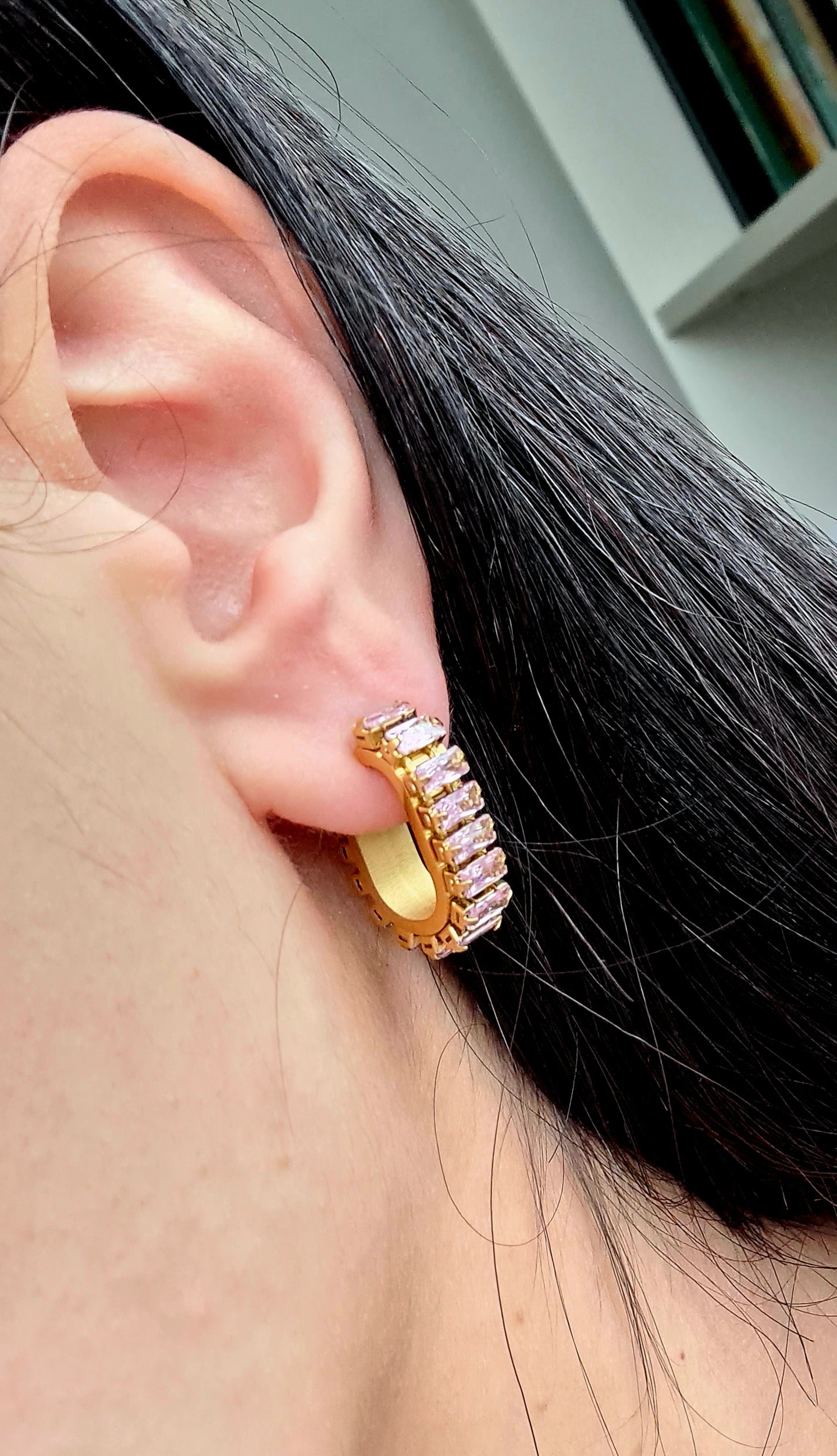 a woman wearinA pair of gold geometric design hoop earrings with pink cubic zirconia stones.