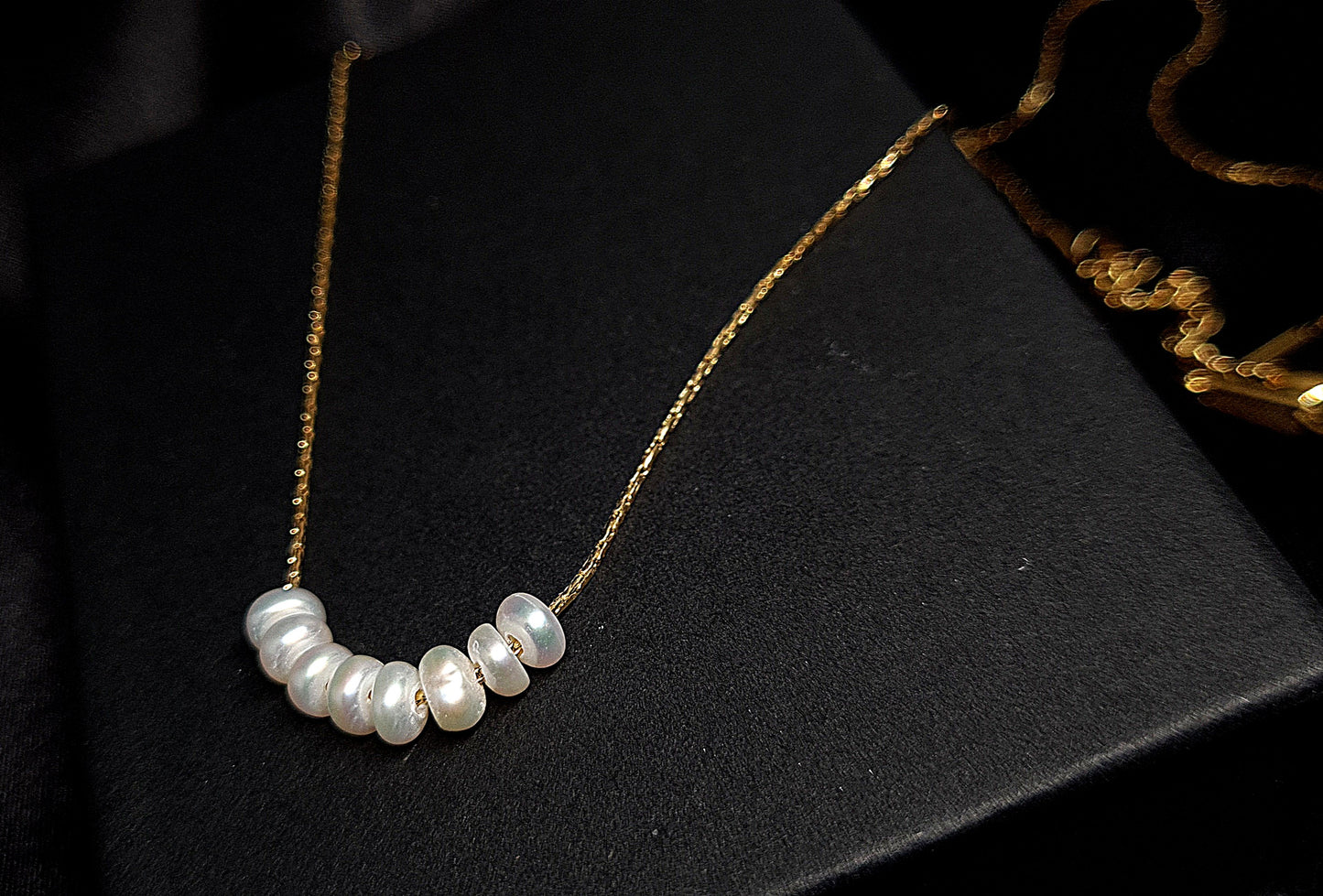 Pearl necklace sitting on black box. The necklace is made of pearls and has a simple design. The pearls are round and white, and they are strung on a black thread. The necklace is sitting on a black box, which provides a nice contrast to the white color of the pearls.