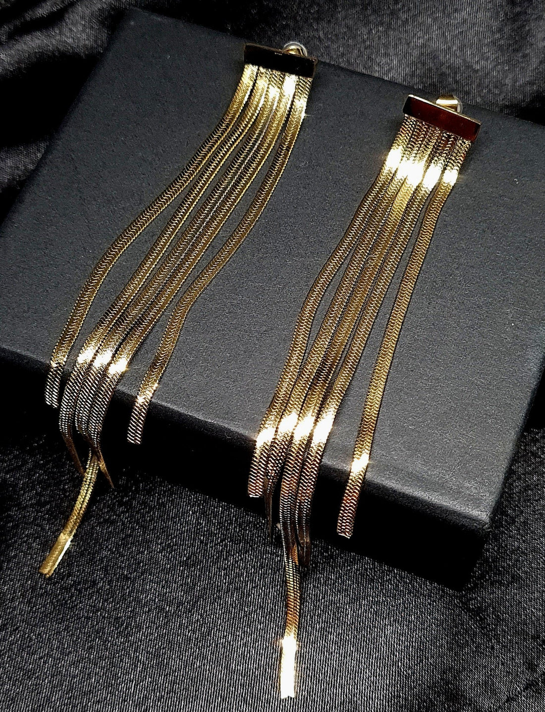 a golden dangle chain earrings showcased on black jewelry box