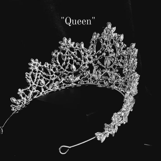 a video of a A silver tiara with a teardrop-shaped center stone and a design of intertwined vines and flowers. The tiara is encrusted with clear cubic zirconia stones. The tiara is sitting on a black velvet surface.