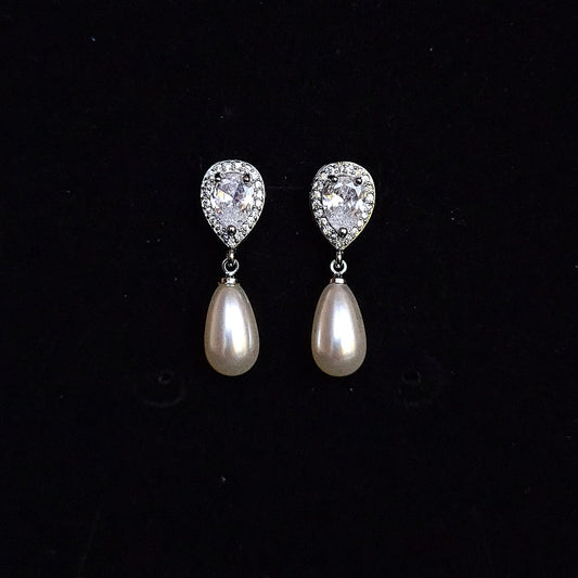 A pair of silver earrings with pearls and diamonds on a black box. The earrings are teardrop-shaped and have a simple, elegant design. The pearls are white and the diamonds are clear.