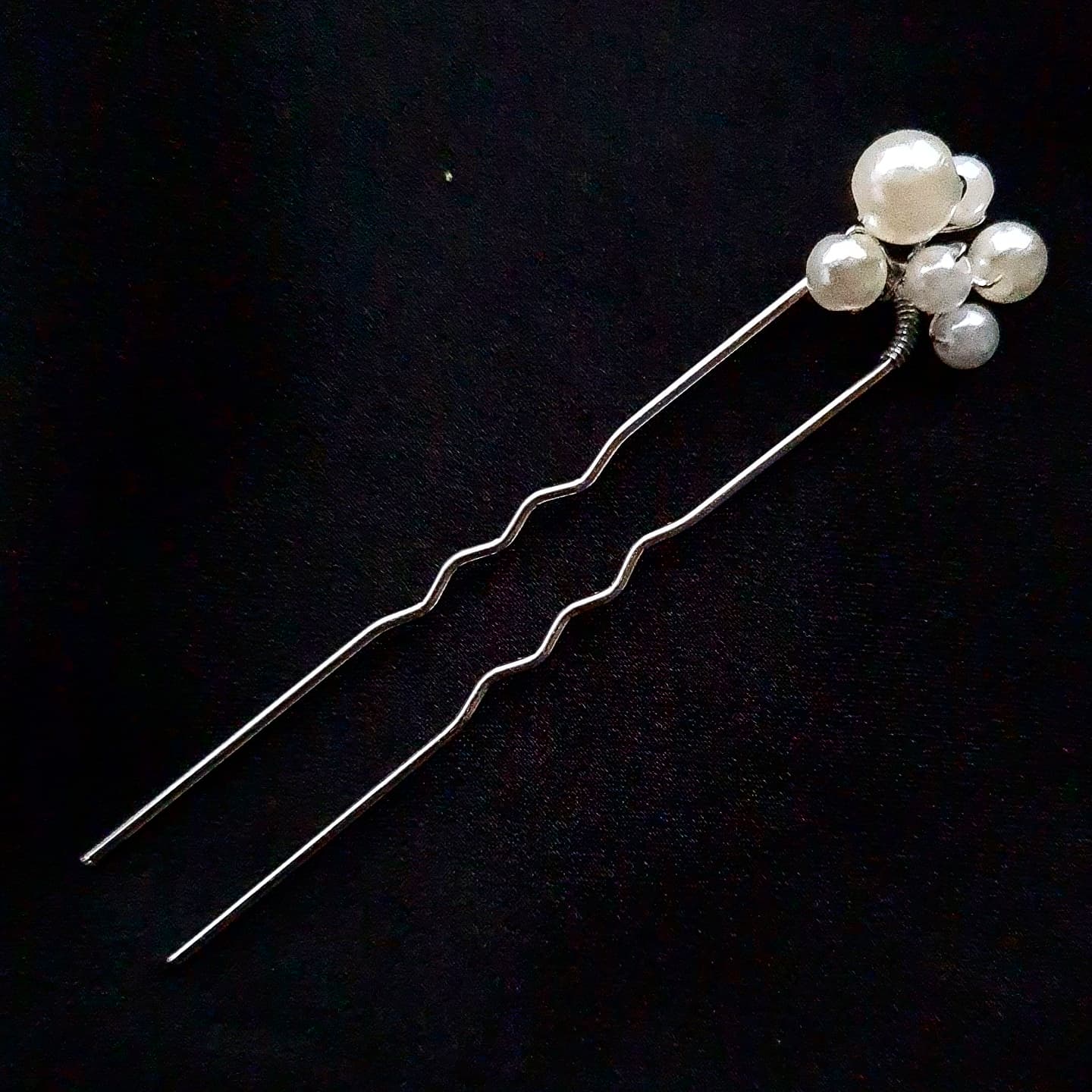 a hair pins with pearls on them. The hair pin is made of metal and have pearls of different sizes on them. The hair pin is in white color.