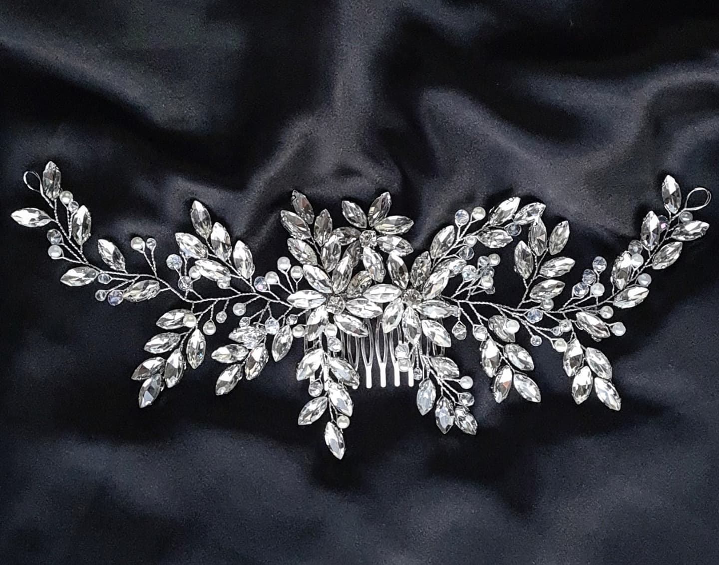 A hair comb with rhinestones and leaves on a black background. It has a delicate design with leaves and flowers. The rhinestones are clear and sparkling. The background is black.