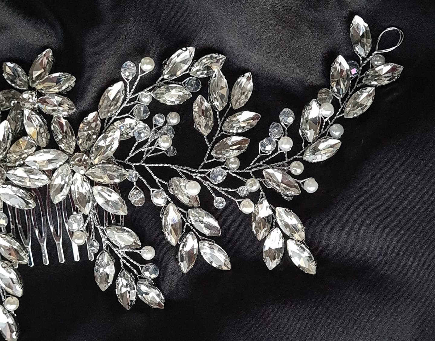 a close up view of A hair comb with rhinestones and leaves on a black background. It has a delicate design with leaves and flowers. The rhinestones are clear and sparkling. The background is black.