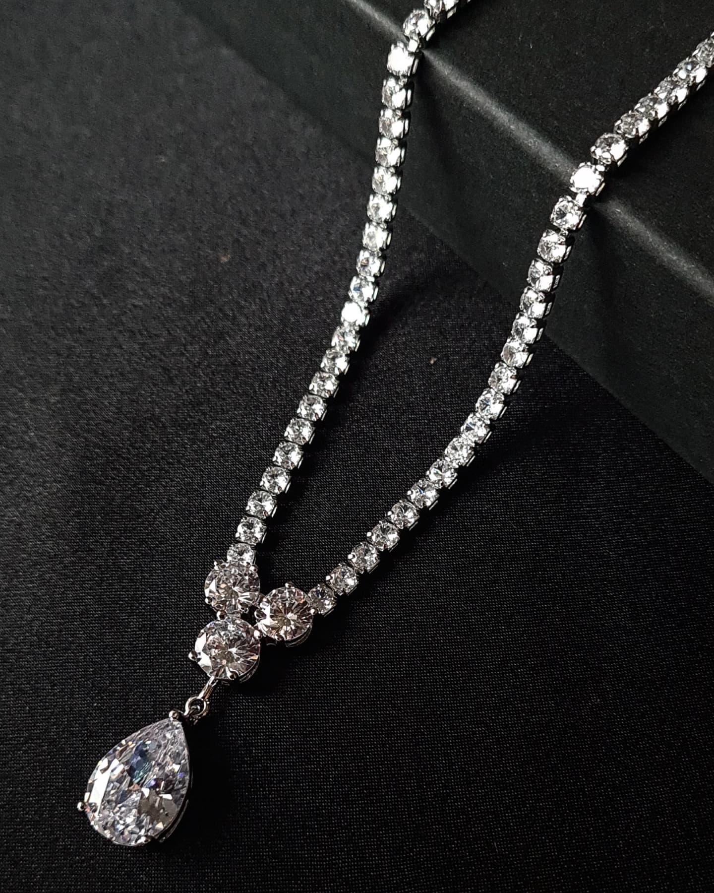 Close-up view of a diamond necklace sparkling with zirconia Diamonds displayed on a black table. the center piece is tear drop shape zirconia stone. 