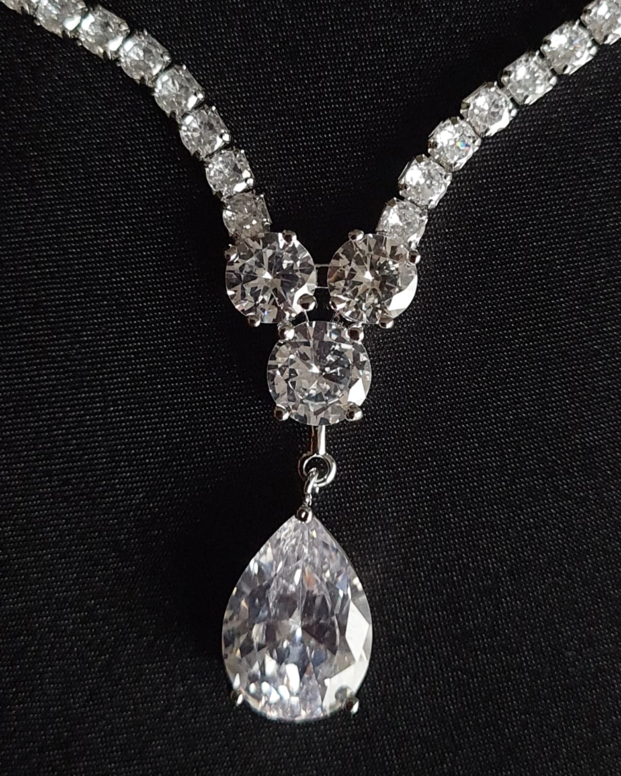 Close-up view of a diamond necklace sparkling with zirconia Diamonds displayed on a black table. the center piece is tear drop shape.