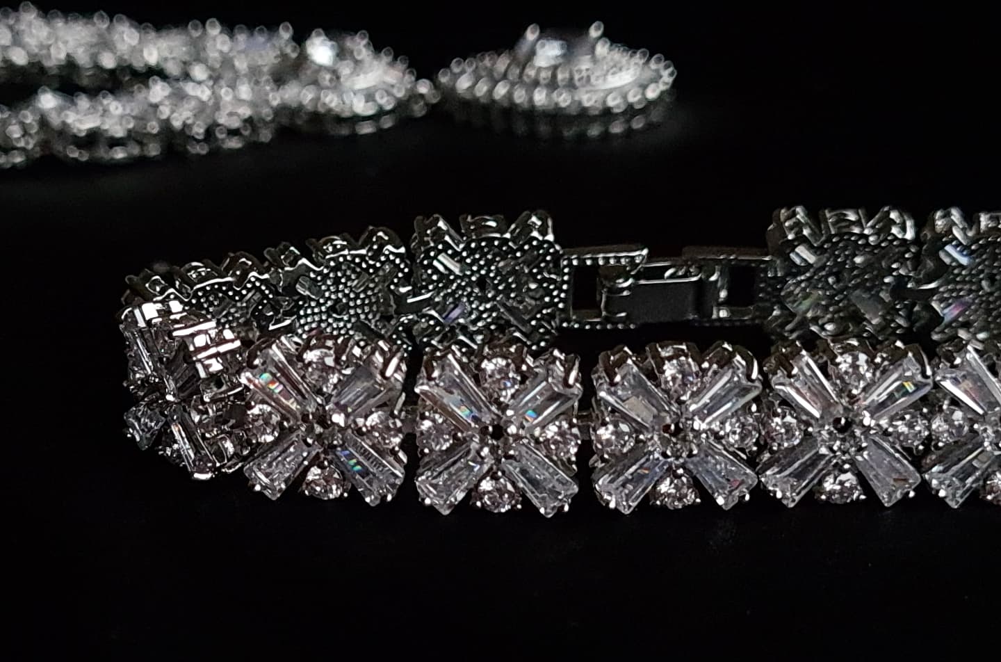  A close-up of a diamond bracelet on a black background. The bracelet is made of silver and has diamonds encrusted on it. The diamonds are sparkling and the bracelet is very shiny.