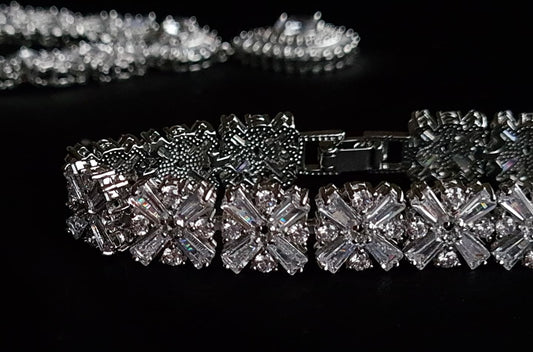 A close-up of a diamond bracelet on a black background. The bracelet is made of silver and has diamonds encrusted on it. The diamonds are sparkling and the bracelet is very shiny.