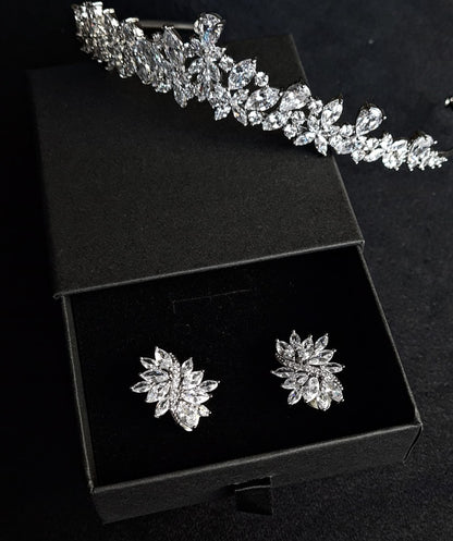 A pair of sterling silver stud earrings with cubic zirconia stones. The earrings are flower-shaped and have a delicate, intricate design. The cubic zirconia stones are clear and sparkling. The earrings are sitting on a black velvet surface. a cubic zirconia tiara next to the box.