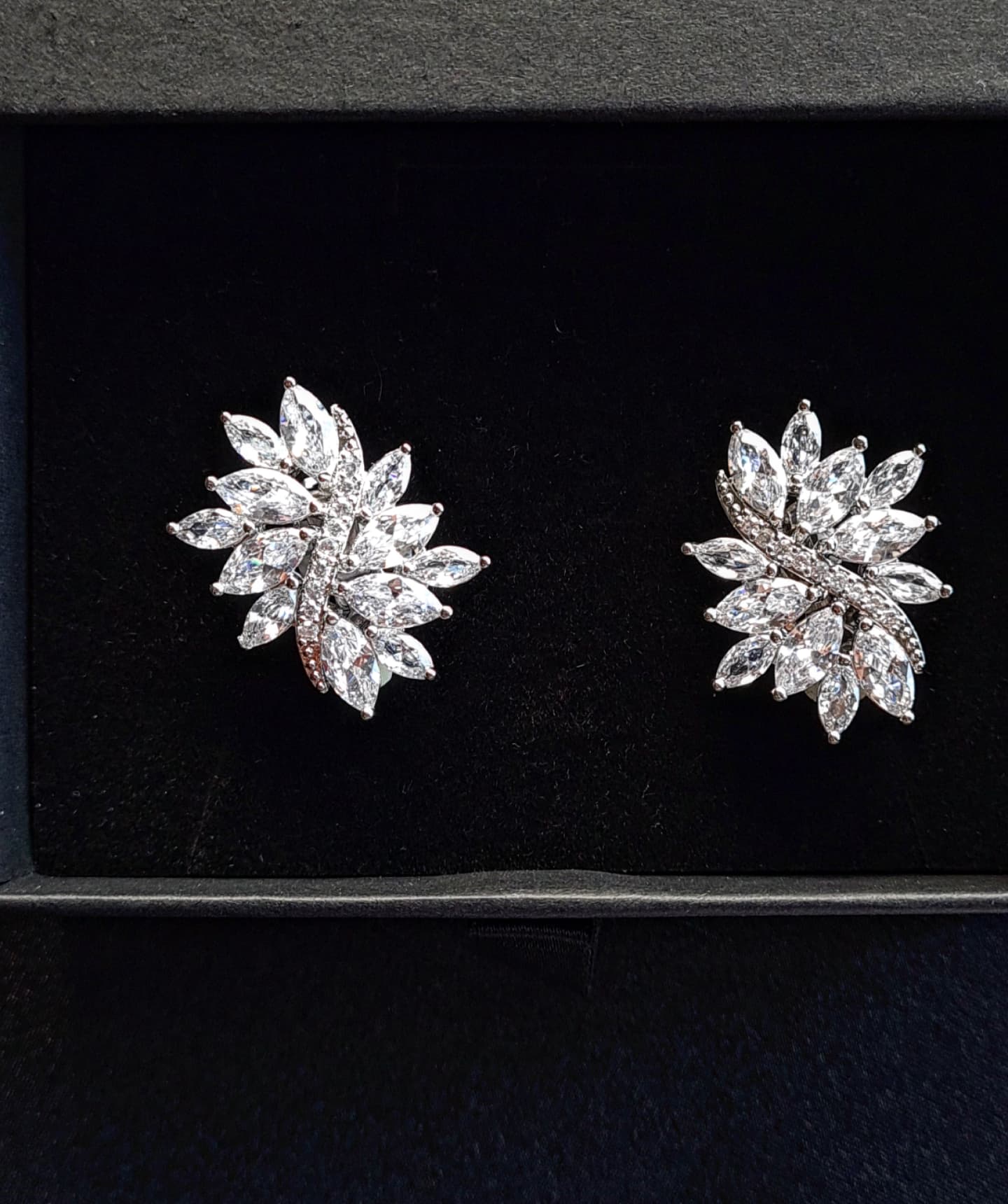 A pair of sterling silver stud earrings with cubic zirconia stones. The earrings are flower-shaped and have a delicate, intricate design. The cubic zirconia stones are clear and sparkling. The earrings are sitting on a black velvet surface.