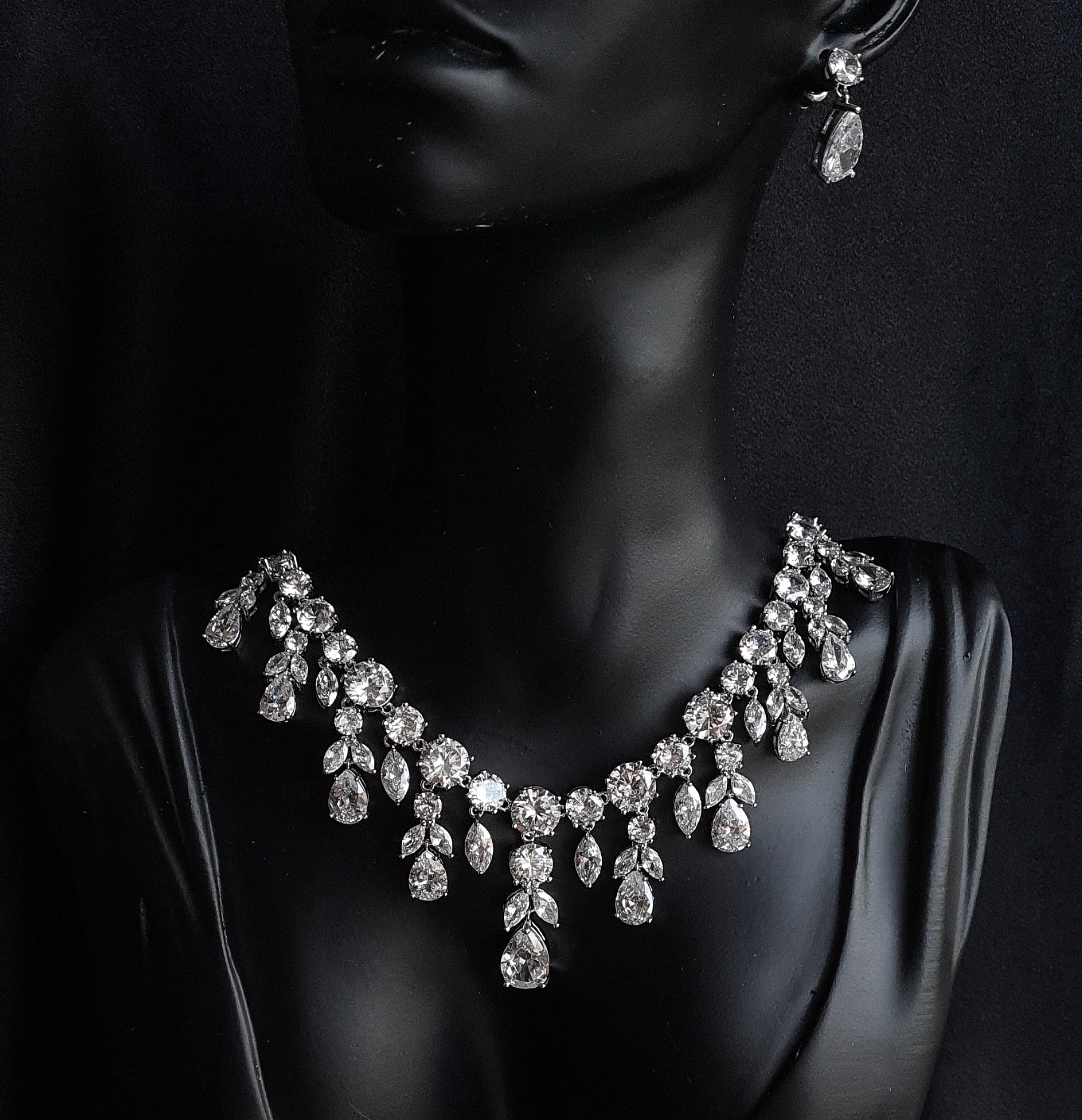 Image of a bridal necklace and earrings set on a mannequin. The necklace is made of cubic zirconia and features a large, round pendant in teardrop shape The earrings are also made of cubic zirconia and have a teardrop shape.