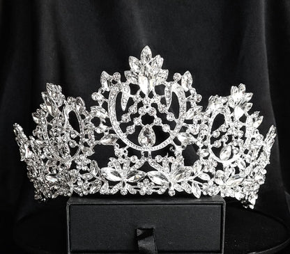 A silver tiara with a teardrop-shaped center stone and a design of intertwined vines and flowers. The tiara is encrusted with clear cubic zirconia stones. The tiara is sitting on a black velvet surface.