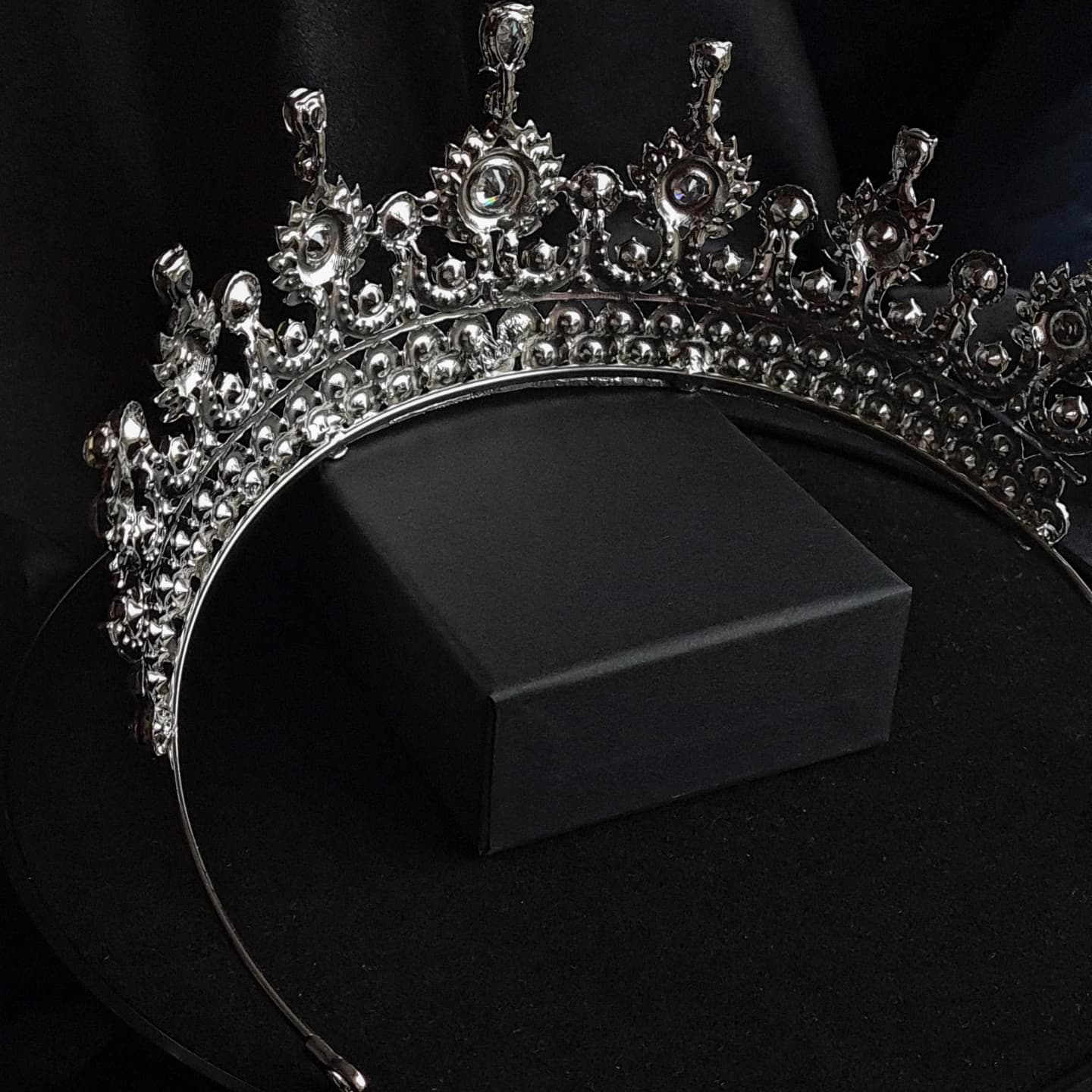 a back view of A close-up of a tiara with rhinestones on a black background. The tiara is made of silver and features a delicate design with cascading rhinestones. The rhinestones are clear and sparkling.