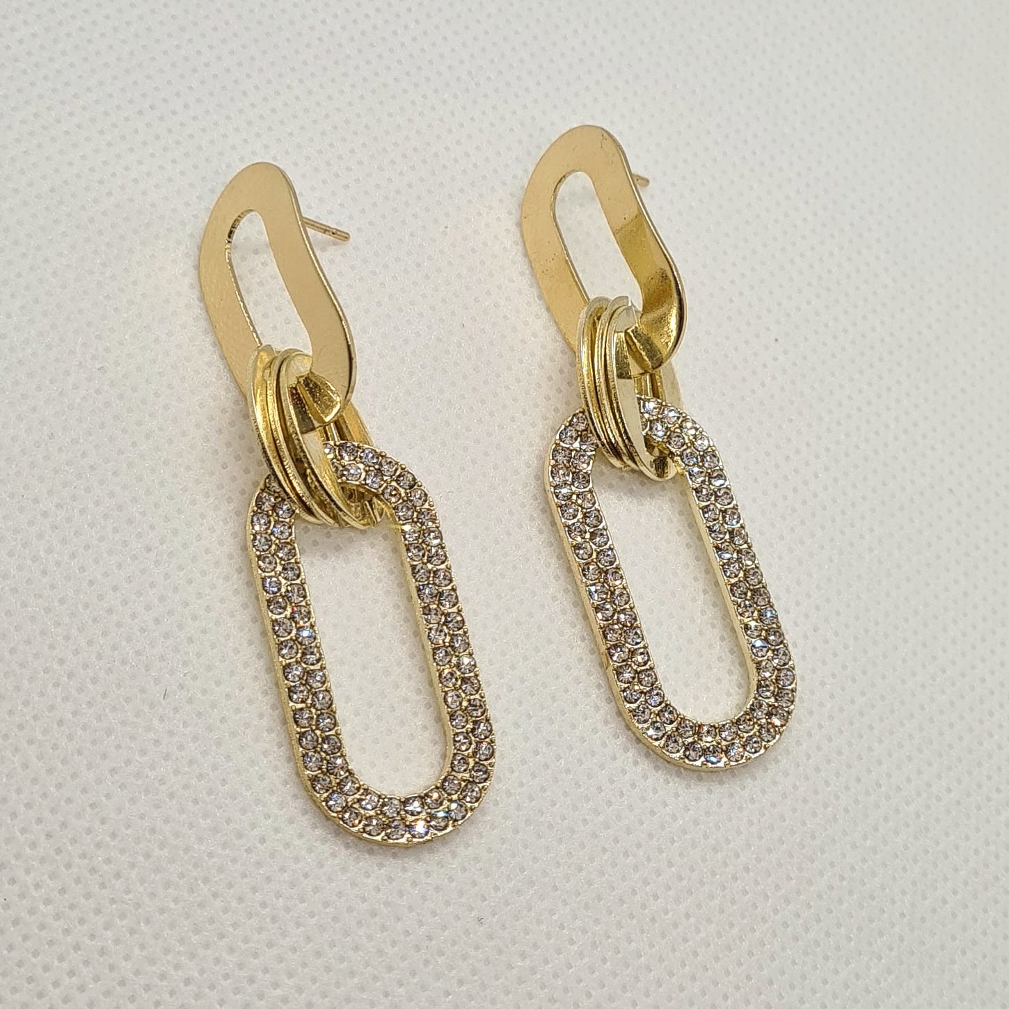 A pair of gold earrings with rhinestones on a white background. The earrings are teardrop-shaped with a gold border. The rhinestones are clear and round. The background is a white.