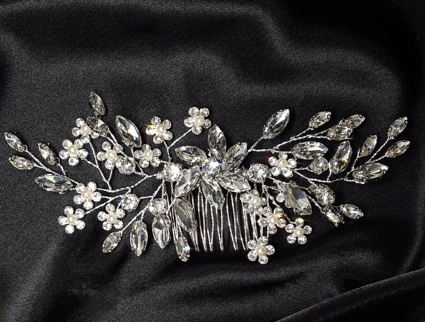 A hair comb with crystals and flowers on a black background. It has a delicate design with flowers and leaves. The crystals are clear and sparkling. The background is black.