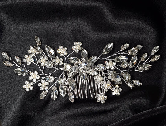 A hair comb with crystals and flowers on a black background. It has a delicate design with flowers and leaves. The crystals are clear and sparkling. The background is black.