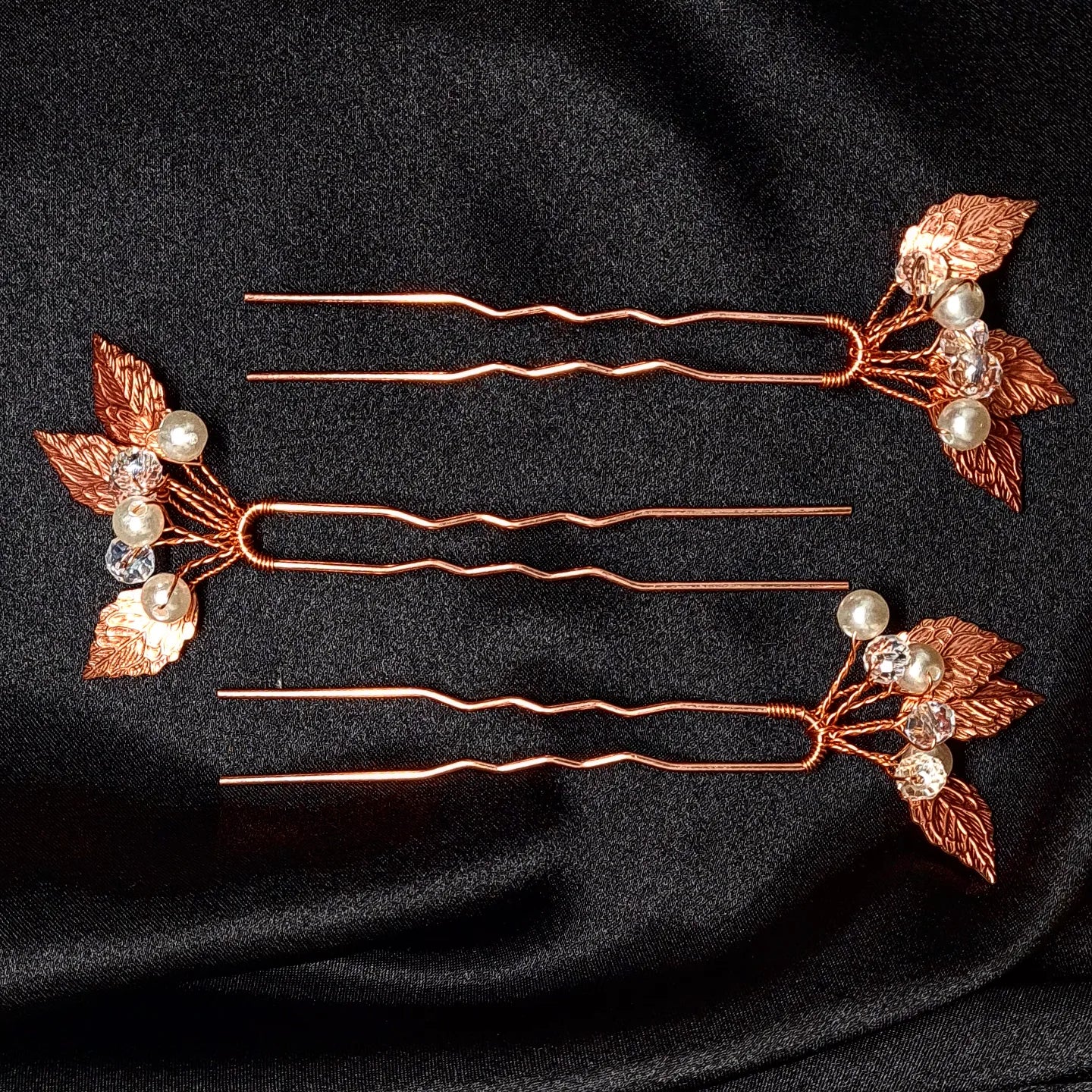 a set of three hair pins with leaves and pearls. The hair pins are made of copper and have pearls and leaves on them. The hair pins are in rose gold color.