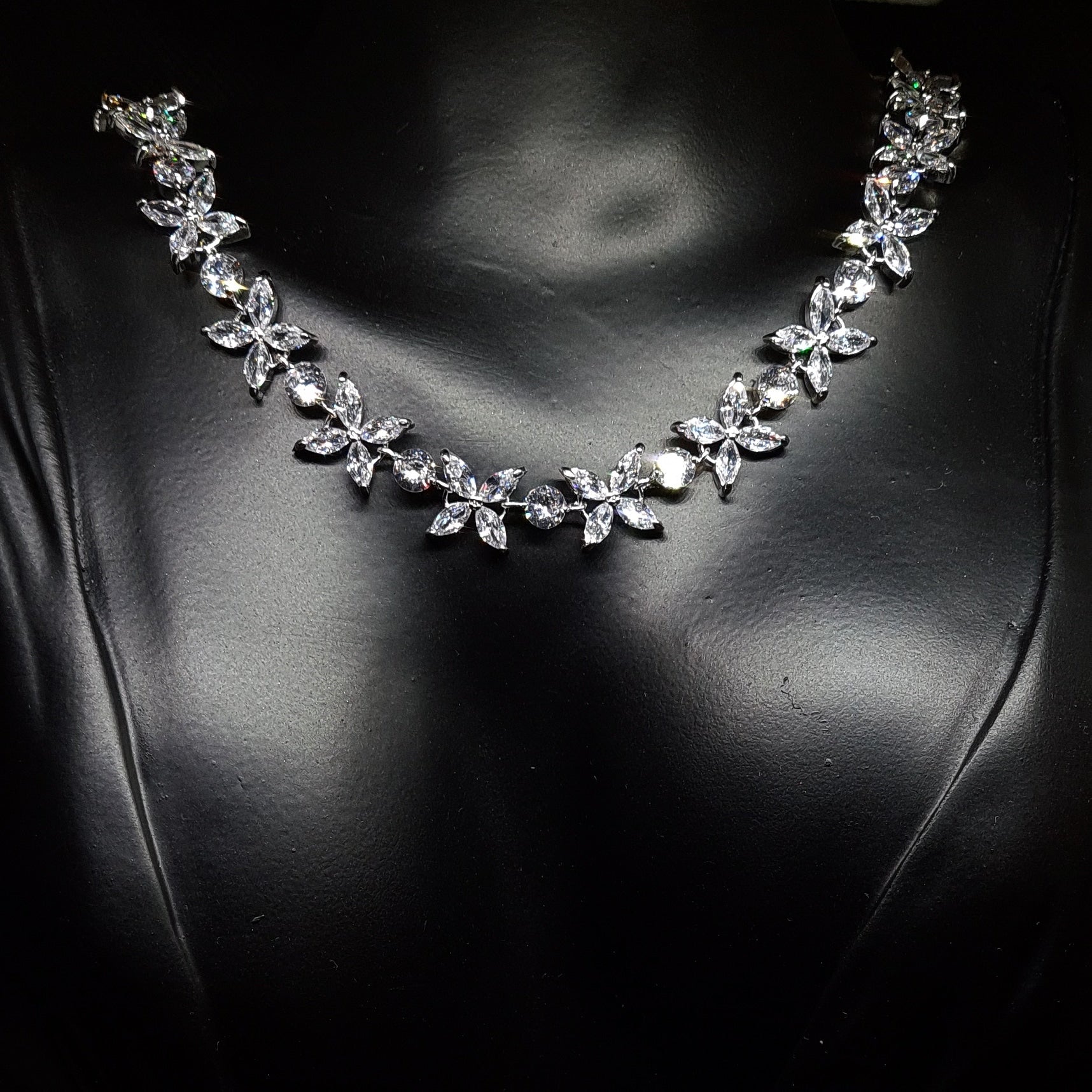 Close-up of a necklace on a mannequin. The necklace is made up of multiple strands of cubic zirconia, with a large pendant in the center. The pendant is flower-shaped and has a sparkling cubic zirconia in the center. The necklace is resting on the mannequin's neck, 