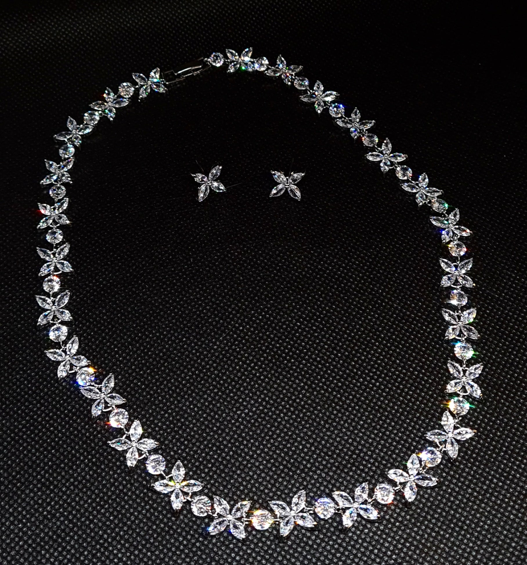 Close-up of a necklace on a mannequin. The necklace is made up of multiple strands of cubic zirconia, with a large pendant in the center. The pendant is flower-shaped and has a sparkling cubic zirconia in the center. The necklace is resting on the mannequin's neck, with matching earrings.