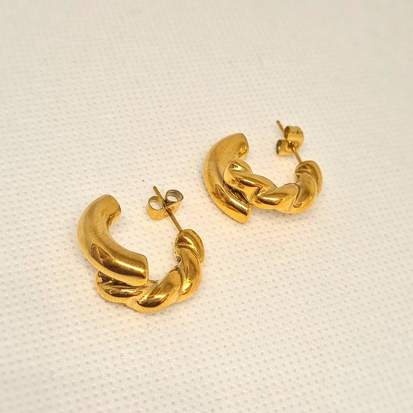 Gold hoop earrings sitting on white surface. The earrings are a classic and elegant style that would be perfect for any occasion. The earrings are made of gold and have a hoop design. The hoops are large and round, and they sit on a white surface.