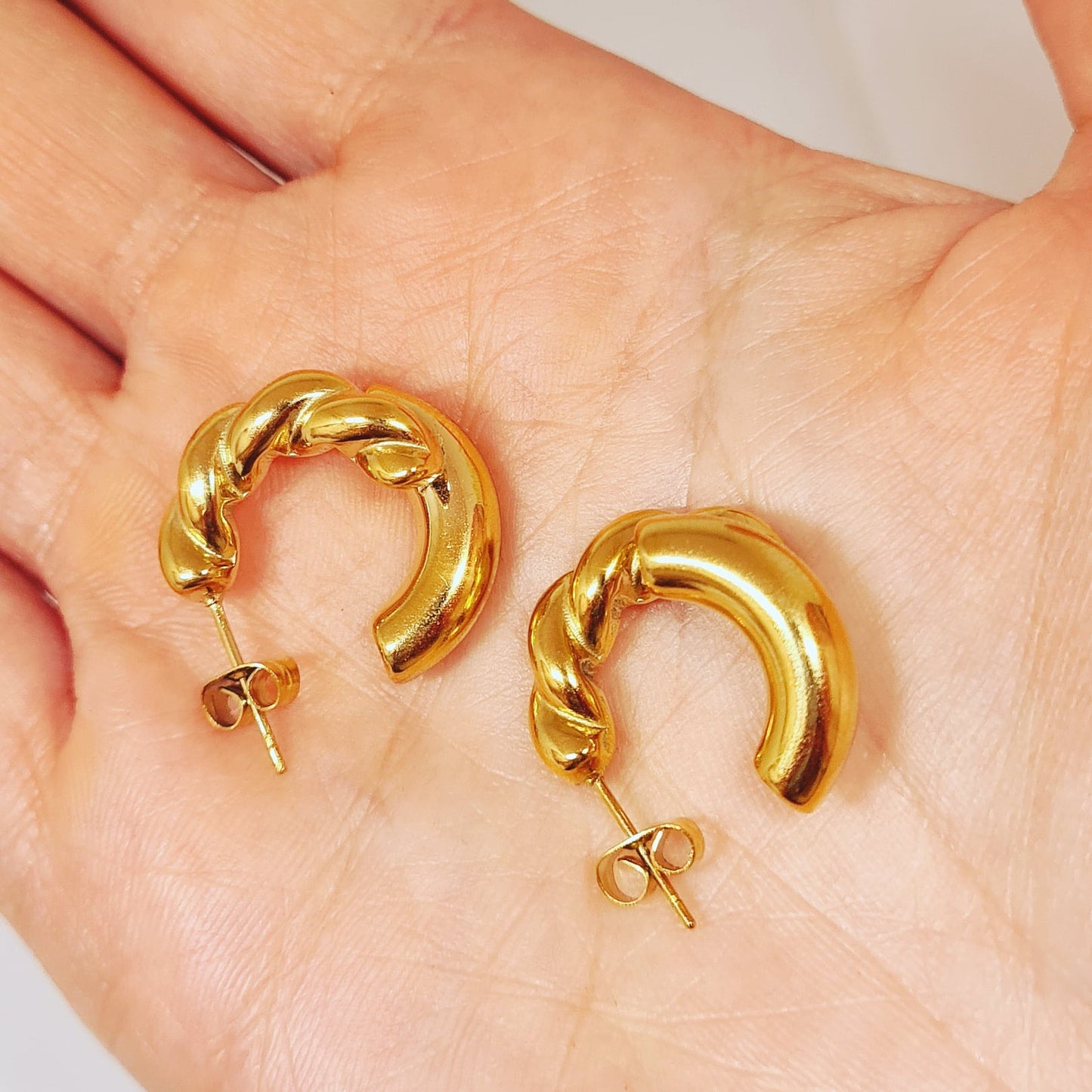 a hand holding Gold hoop earrings. The earrings are a classic and elegant style that would be perfect for any occasion. The earrings are made of gold and have a hoop design. The hoops are large and round.