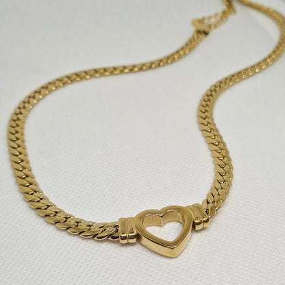 Gold necklace with heart pendant on white background. The necklace is made of gold and has a heart pendant in the center. The heart is gold and has a smooth surface. The necklace is sitting on a white background, which provides a nice contrast to the gold color of the heart