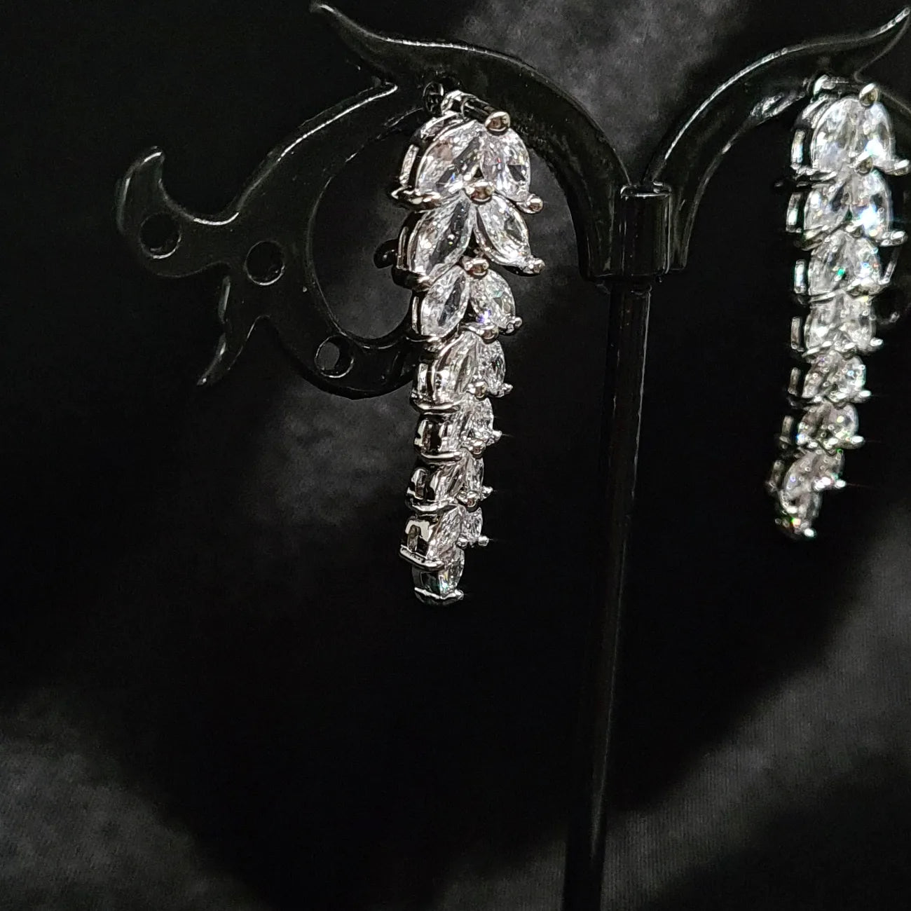 A pair of dangle earrings made of cubic zirconia. The earrings are teardrop-shaped and have a simple, elegant design. The cubic zirconia stones are clear and sparkling. The earrings are sitting on a black cloth.