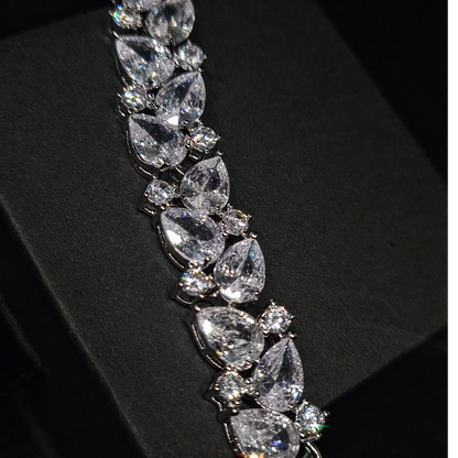 A close-up of a silver bracelet with diamonds on a black background. The bracelet has a intricate design with a double row of diamonds. The diamonds are sparkling and the bracelet is very shiny.