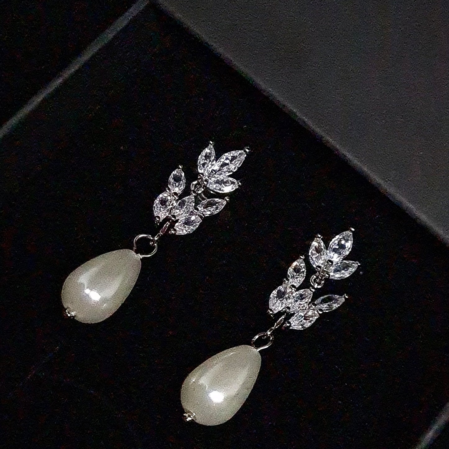 A pair of earrings made of pearl and rhinestones on a black box. The earrings are decorated with a pearl and rhinestones. The earrings are perfect for a special occasion or for everyday wear