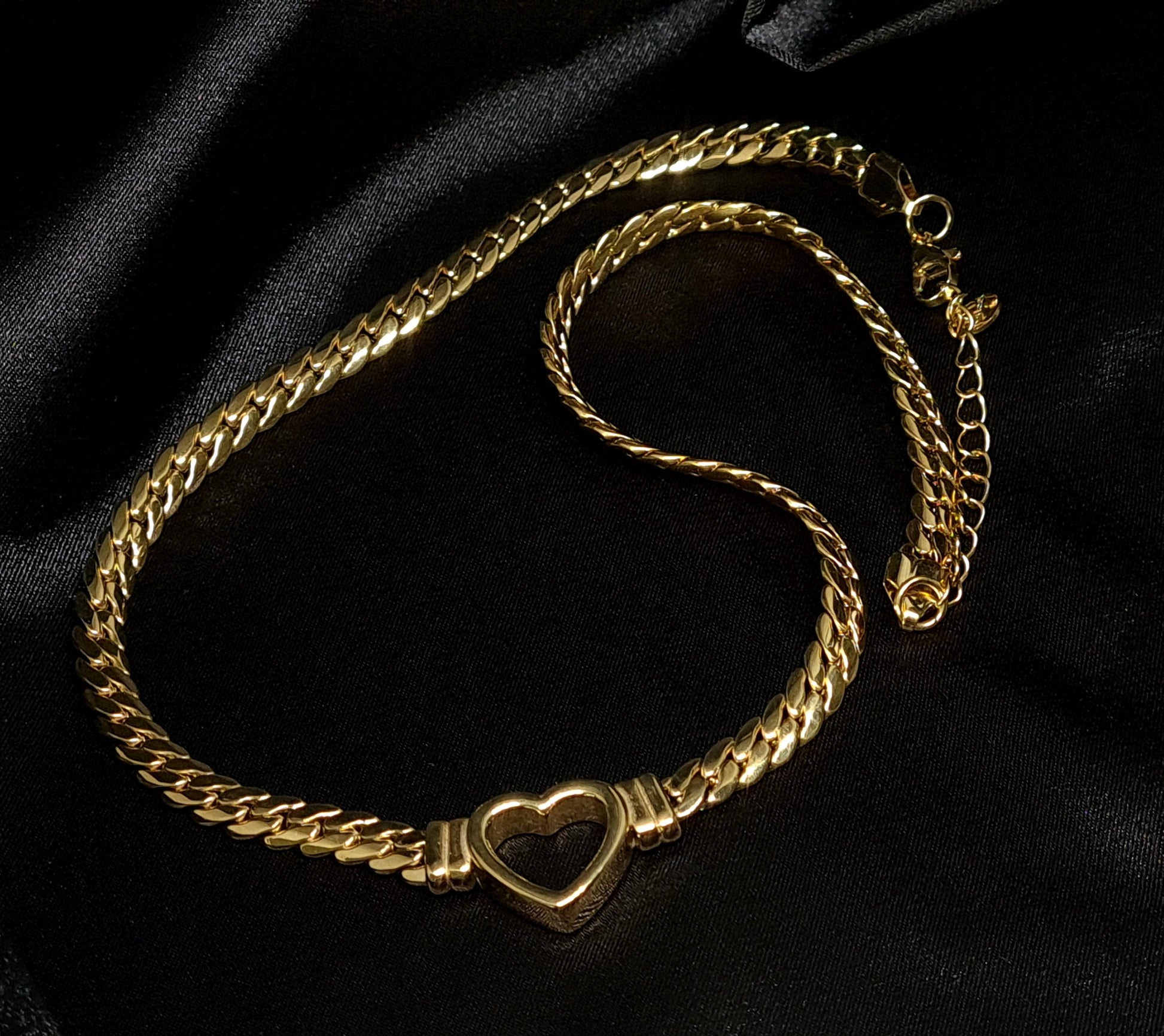 Gold curb chain necklace featuring a minimalist open-heart pendant, displayed on a premium black silk background for a luxury jewelry launch.